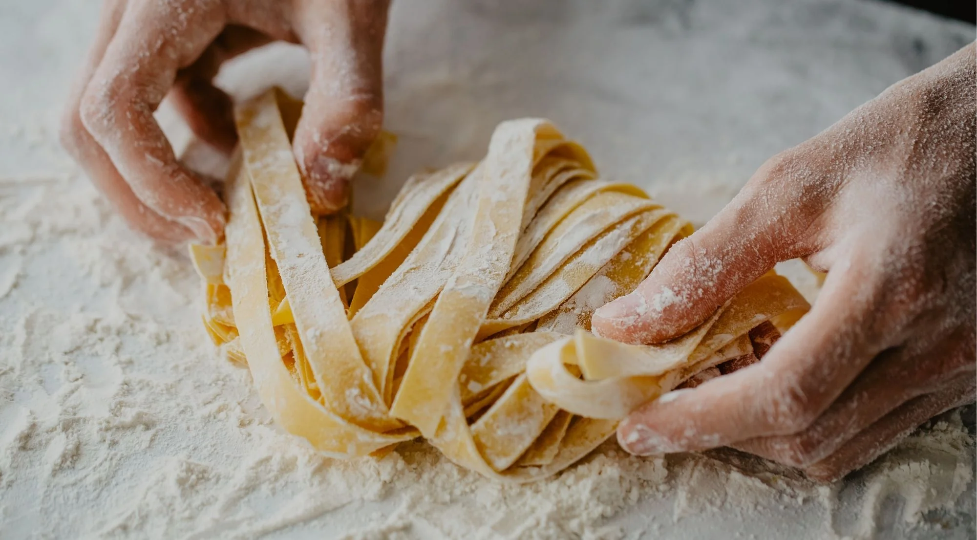 Hands shaping fresh tagliatelle pasta on a floured board during a Naples cooking class
