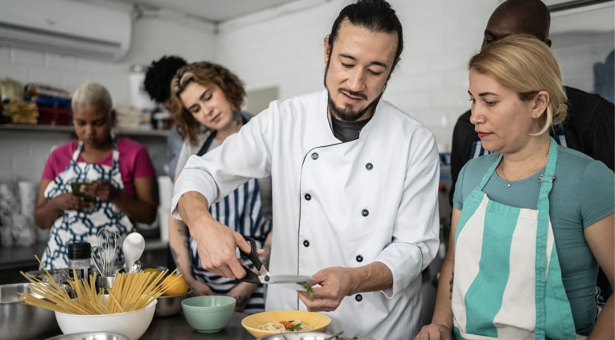 Local chef in white coat guiding cooking class students in a professional kitchen in Naples